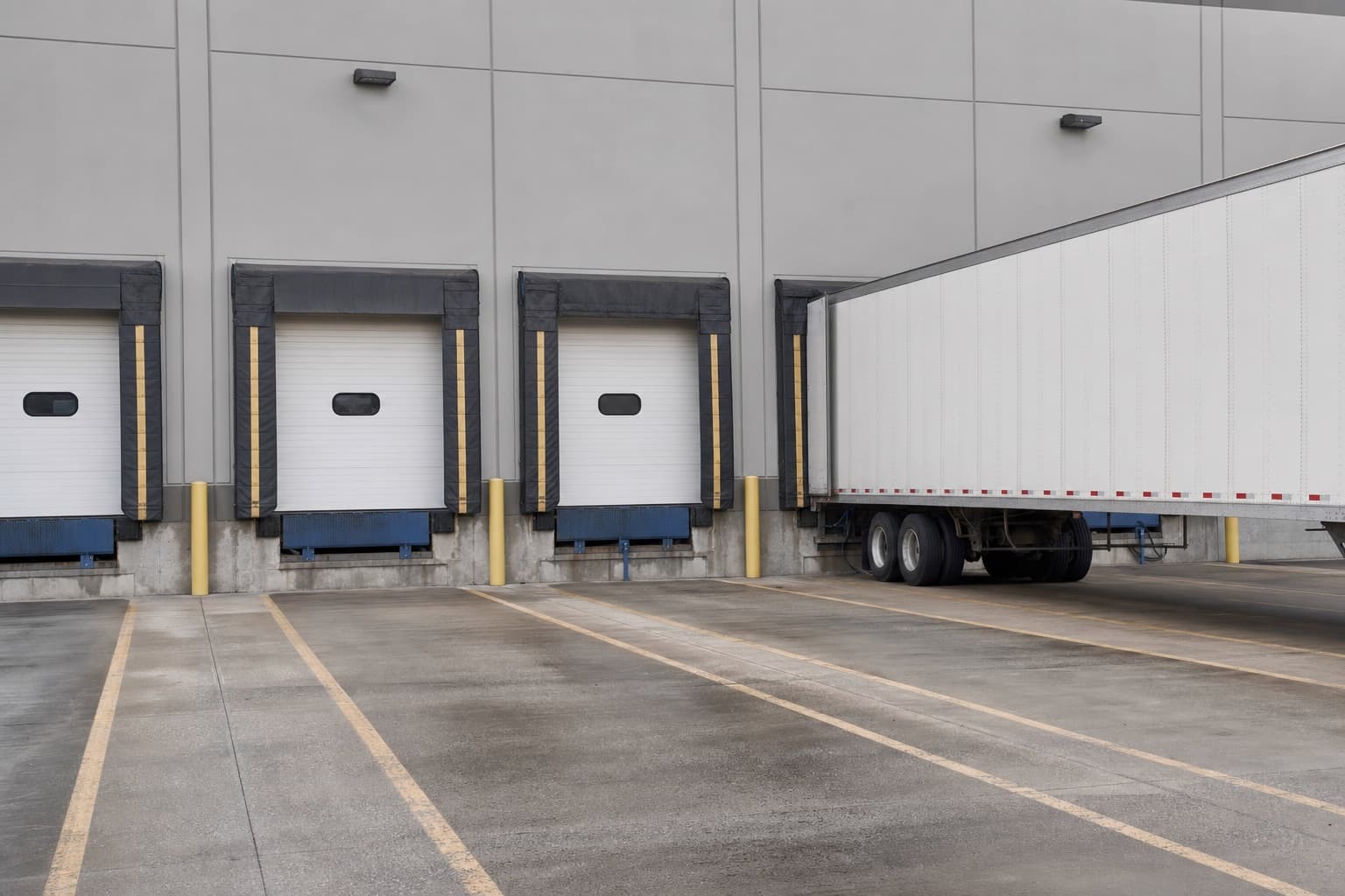 A loading dock seen from the yard, a trailer reversing in between painted lane markings